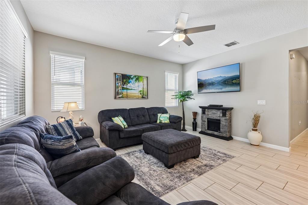 A living room features dark gray sofas, a matching ottoman, a fireplace, and tile flooring — 8077 CHERRYSTONE STREET, LEESBURG, FL