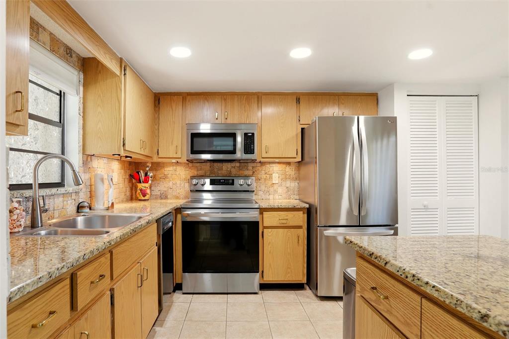 A kitchen with light wood cabinets, granite countertops, stainless steel appliances, and a tiled backsplash — 1400 1ST AVENUE W UNIT 203, BRADENTON, FL
