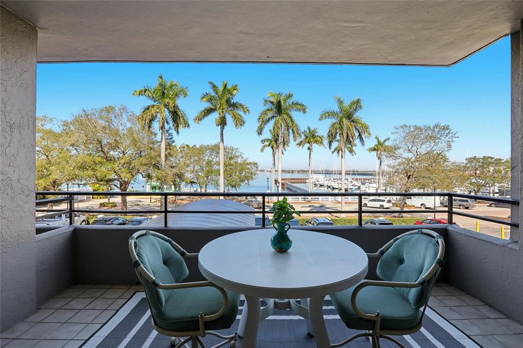 A balcony with a table and two chairs overlooks a marina and palm trees — 1400 1ST AVENUE W UNIT 203, BRADENTON, FL