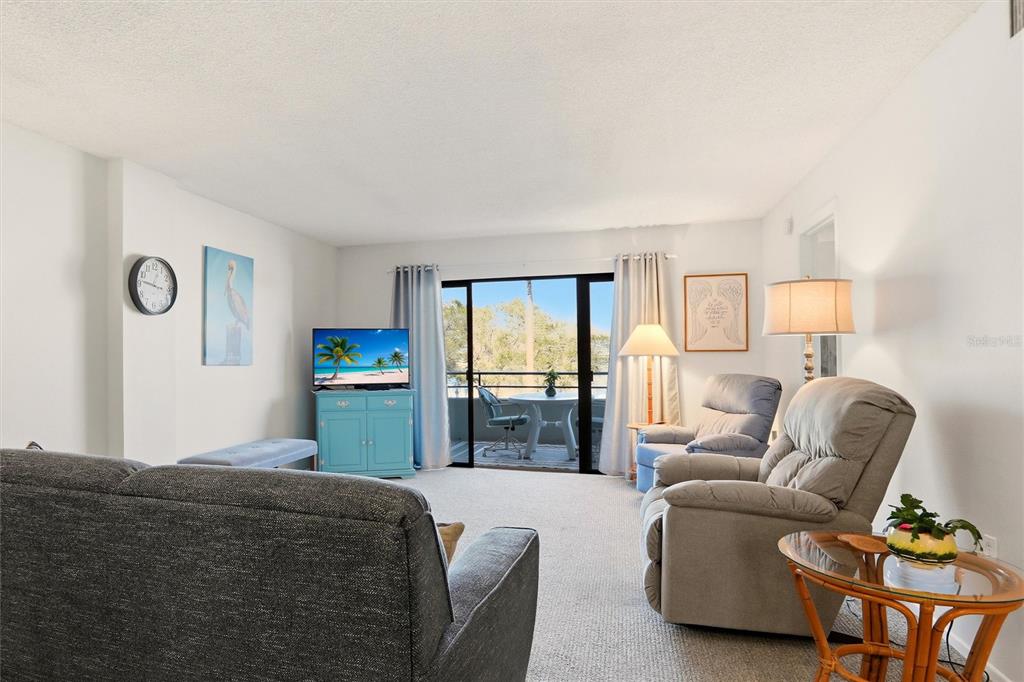 A living room features a grey sofa, two recliners, a blue cabinet, and a balcony view — 1400 1ST AVENUE W UNIT 203, BRADENTON, FL