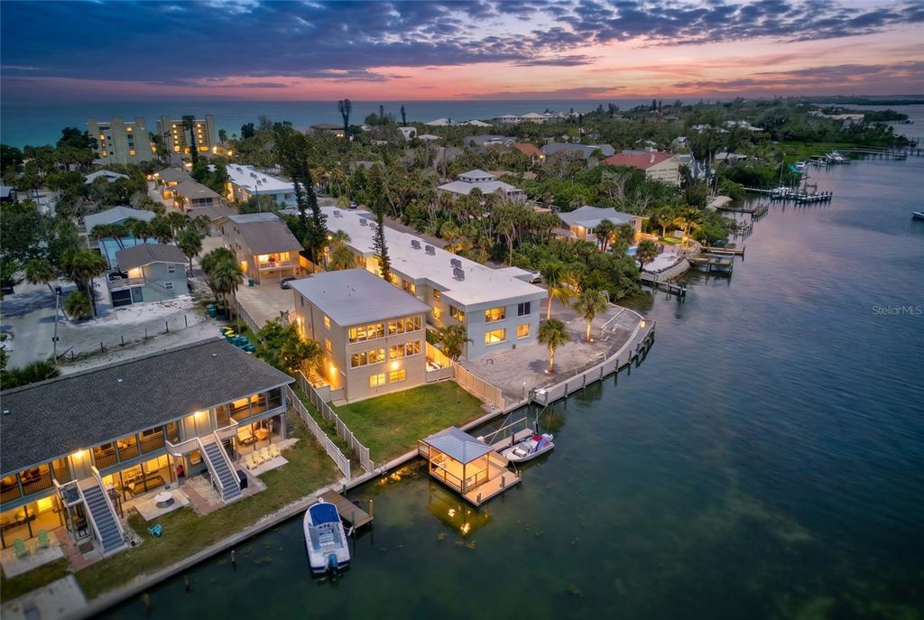 An aerial view shows waterfront multi-story buildings with docks, boats, and palm trees at sunset — 5055 N BEACH ROAD UNIT 101, ENGLEWOOD, FL