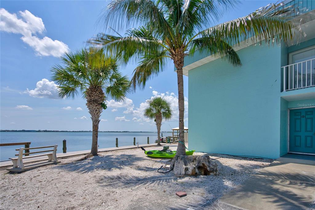 A light blue building exterior sits beside a sandy waterfront area with palm trees — 5055 N BEACH ROAD UNIT 101, ENGLEWOOD, FL