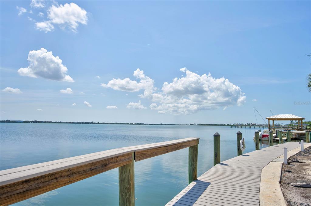A wooden dock with a railing extends over calm water toward a small boat shelter — 5055 N BEACH ROAD UNIT 101, ENGLEWOOD, FL
