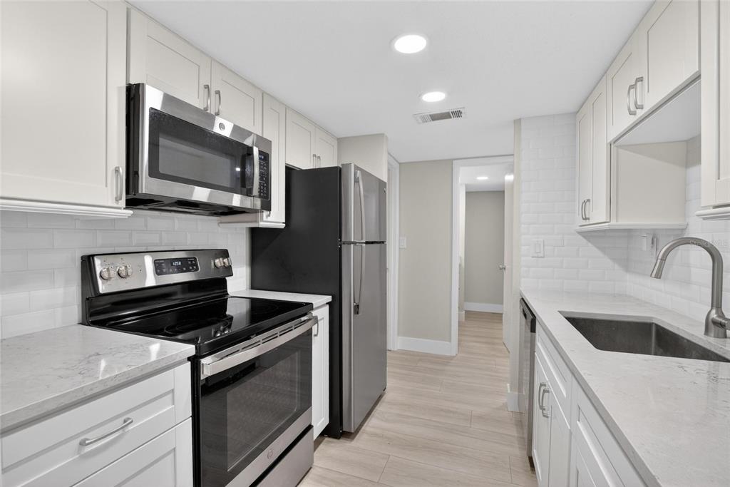 A galley kitchen features white cabinets, light countertops, subway tile backsplash, and stainless steel appliances — 3795 41ST LANE S UNIT A, ST PETERSBURG, FL