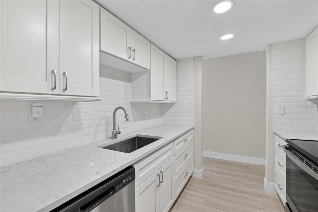 A modern kitchen features white cabinets, marble-look countertops, a stainless steel sink, and subway tile — 3795 41ST LANE S UNIT A, ST PETERSBURG, FL