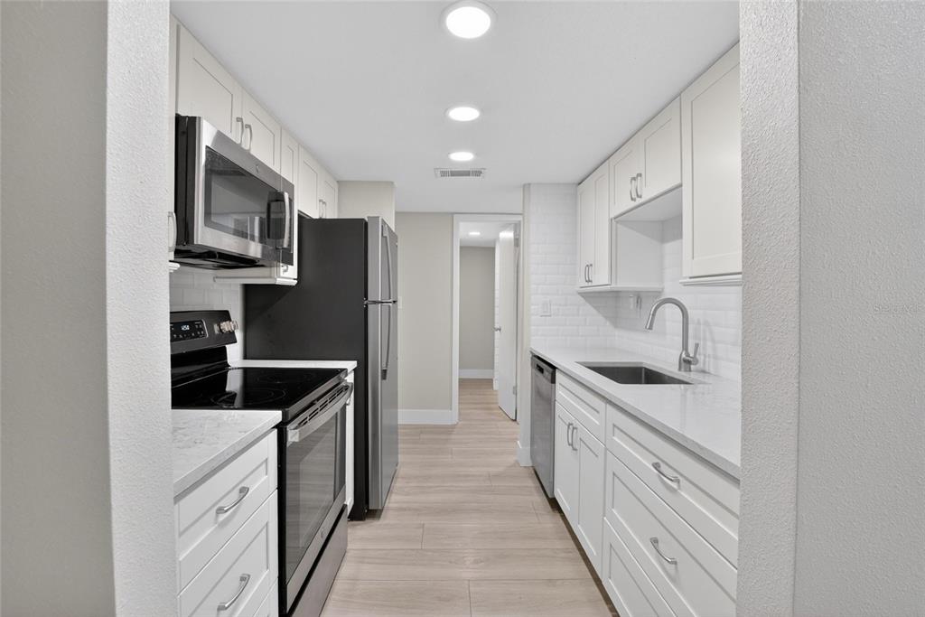 A galley kitchen features white cabinets, stainless steel appliances, and light-colored wood-look flooring — 3795 41ST LANE S UNIT A, ST PETERSBURG, FL