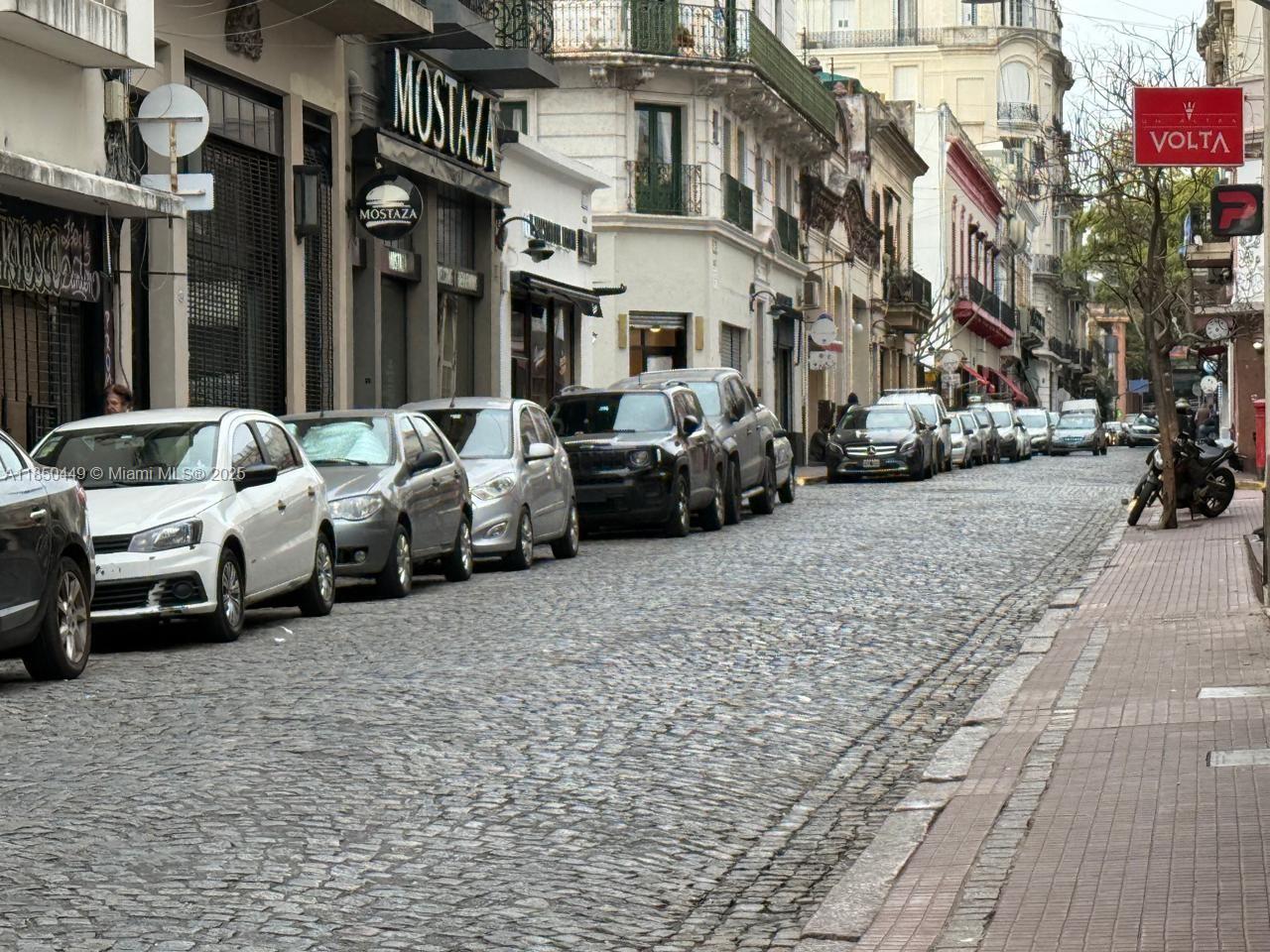 A cobblestone street lined with parked cars and historic buildings featuring a Mostaza restaurant sign — 945 Defensa St San Telmo, FL 945, FL