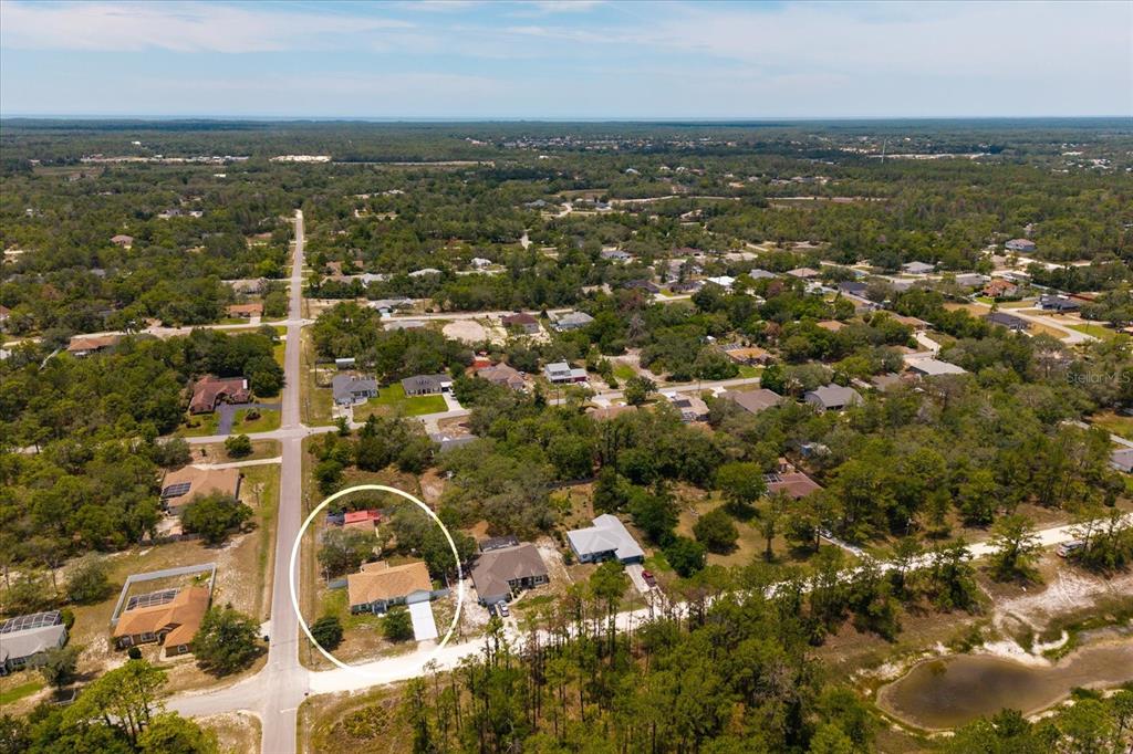 An aerial view shows a single-story house with a tan roof surrounded by wooded lots — 8343 NITTANY ROAD, WEEKI WACHEE, FL