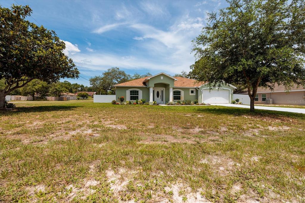 A single-story light green house with a two-car garage sits on a large grassy lot — 8343 NITTANY ROAD, WEEKI WACHEE, FL