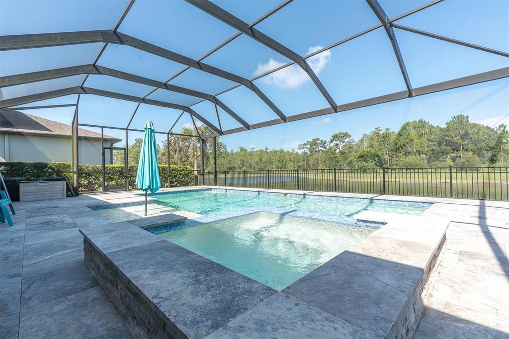 A screened-in pool area features a hot tub, stone decking, and a view of water — 4434 TATUM LOOP, ODESSA, FL
