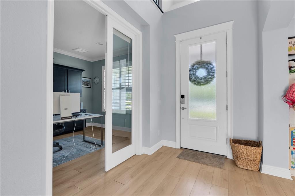 An entryway with light wood flooring leads to a home office through glass-paneled doors — 4434 TATUM LOOP, ODESSA, FL