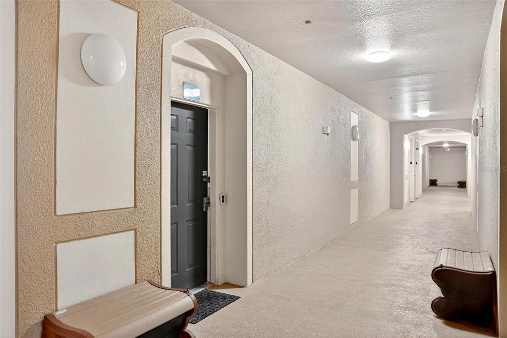 A hallway in an apartment building features a dark door, textured walls, and two benches — 2774 ALMATON LOOP UNIT 105, KISSIMMEE, FL