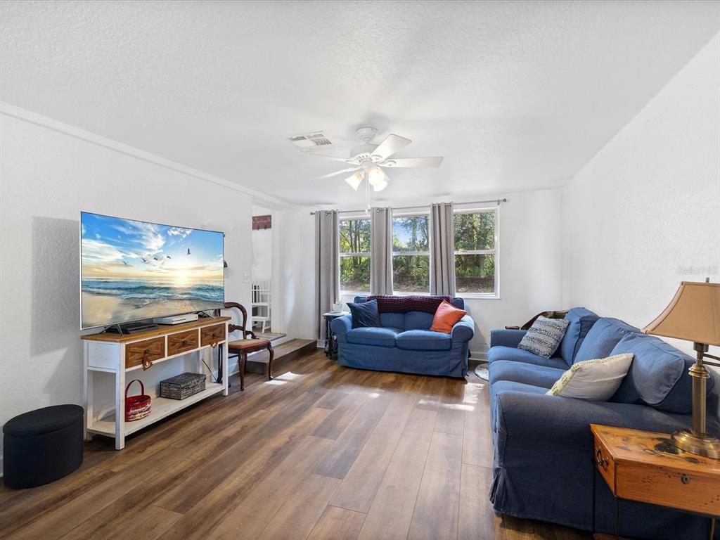 A living room features wood-look flooring, blue sofas, a television on a console, and windows — 36228 CLINTON AVENUE, DADE CITY, FL