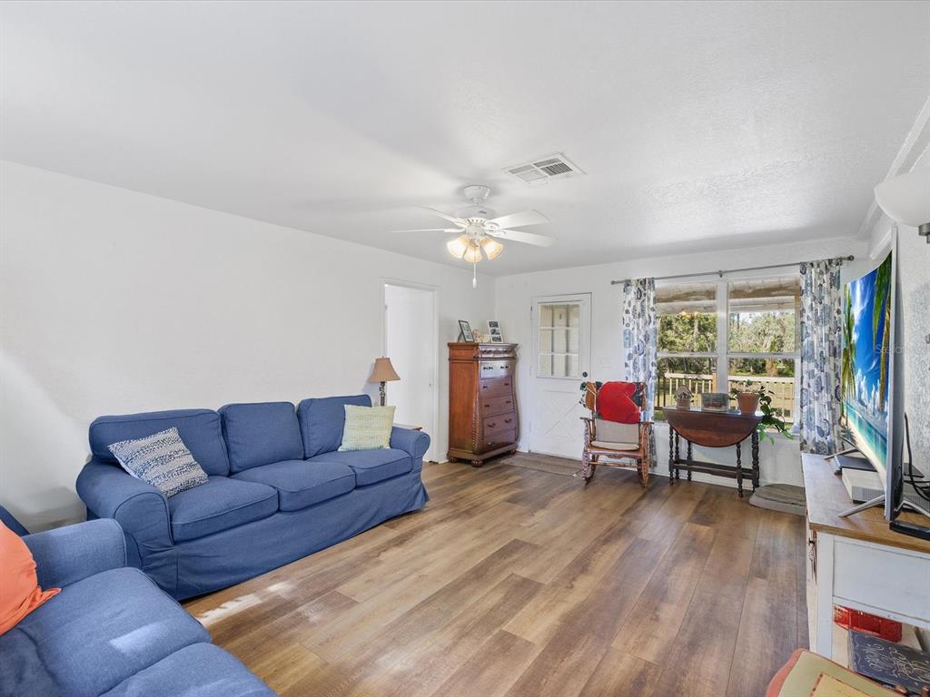 A living room with blue sofas, wood-look flooring, a ceiling fan, and a glass-paned door — 36228 CLINTON AVENUE, DADE CITY, FL