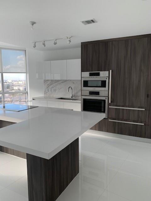 A modern kitchen features a white island, dark wood cabinetry, and stainless steel appliances — 851 NE 1st Ave # 2110, Miami FL 33132, MIAMI, FL