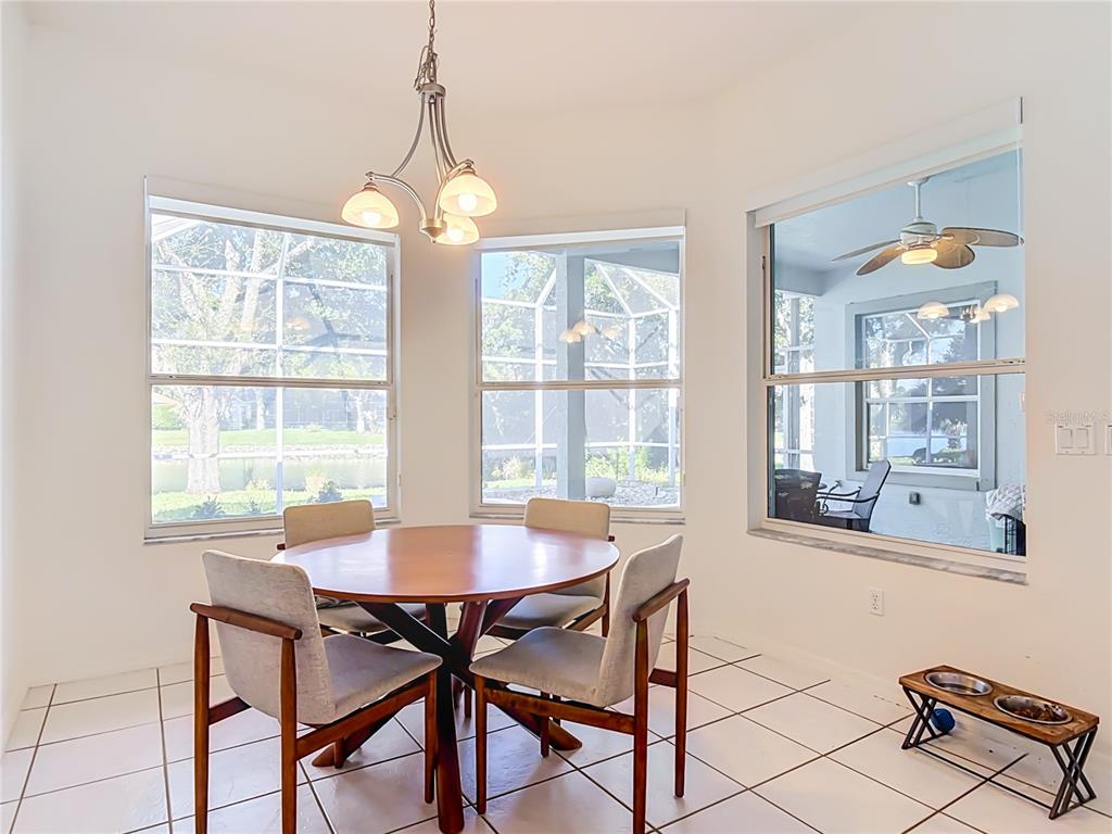 A dining area with a round wooden table, four chairs, tile floors, and large windows — 14 EGRET DRIVE, PALM COAST, FL