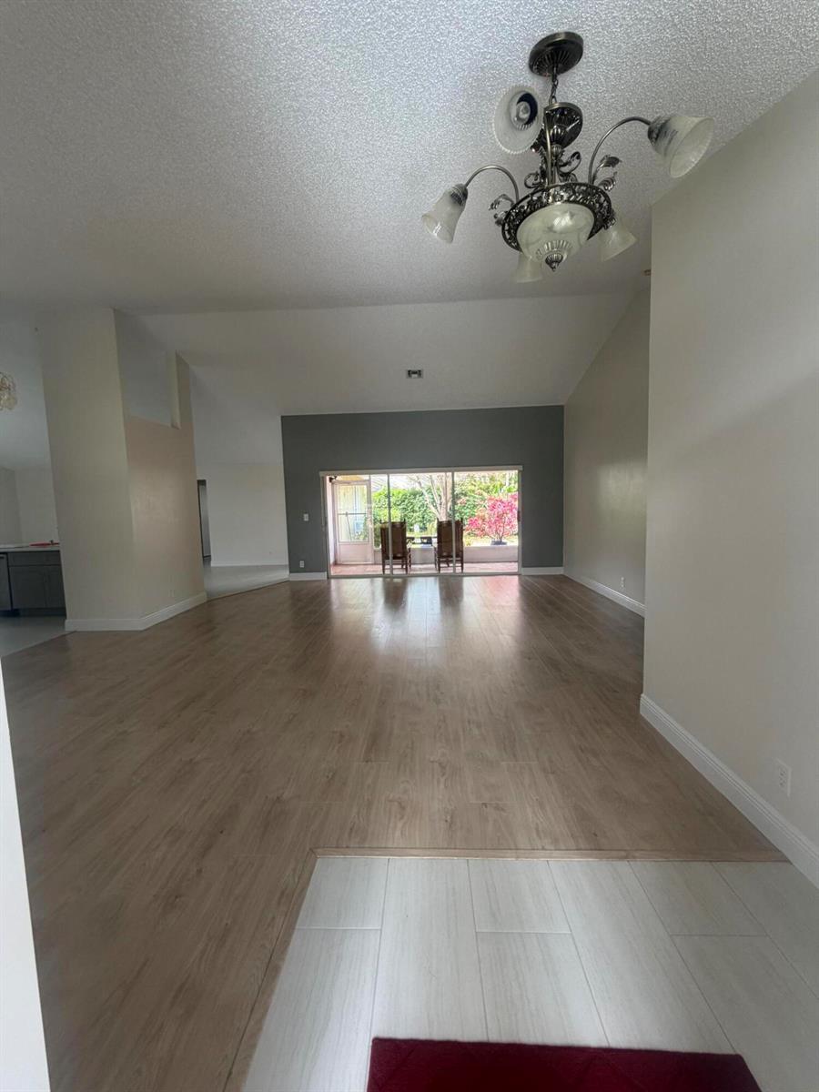 A living area with wood-look flooring, a chandelier, and sliding glass doors to a patio — 1401 Hideaway Bend, Wellington FL 33414, WELLINGTON, FL