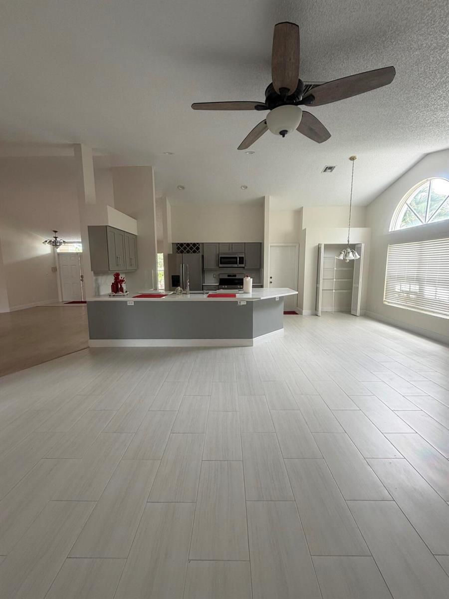 A kitchen with gray cabinets and a breakfast bar overlooks an open-concept living area — 1401 Hideaway Bend, Wellington FL 33414, WELLINGTON, FL