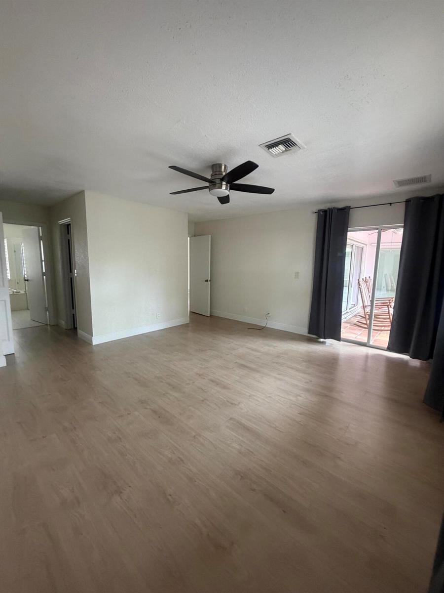 An empty room features light wood-look flooring, a ceiling fan, and sliding glass patio doors — 1401 Hideaway Bend, Wellington FL 33414, WELLINGTON, FL