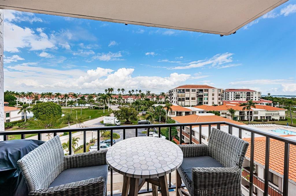 A balcony with a small table and two chairs overlooks a tropical residential complex — 6295 BAHIA DEL MAR CIRCLE UNIT 505, ST PETERSBURG, FL
