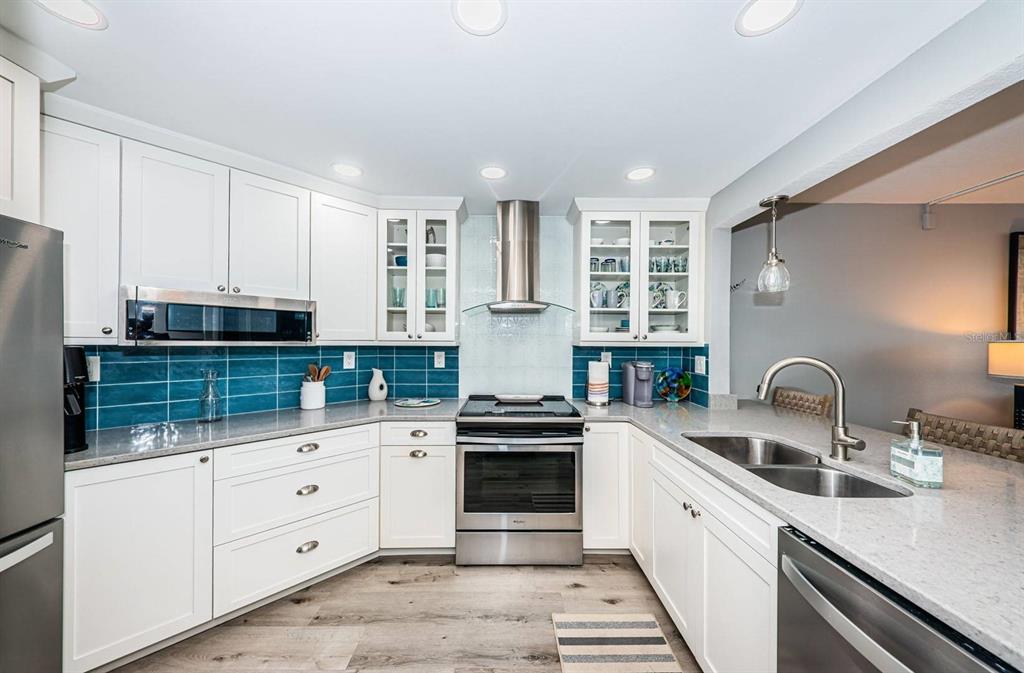 A kitchen with white cabinets, stainless steel appliances, blue tile backsplash, and light countertops — 6295 BAHIA DEL MAR CIRCLE UNIT 505, ST PETERSBURG, FL