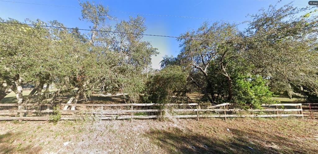 A wooden fence borders a wooded lot with several large trees under a clear sky — GERBER DAIRY RD, WINTER HAVEN, FL