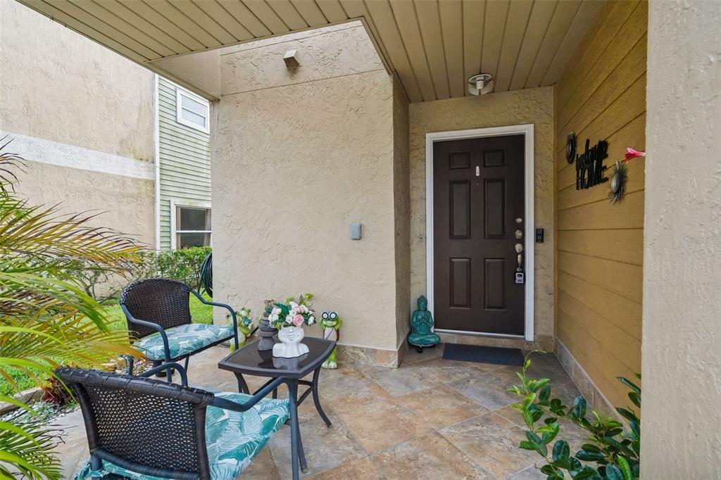 A covered front porch features tiled flooring, two wicker chairs, a small table, and a door — 2448 SUMMERFIELD WAY, KISSIMMEE, FL