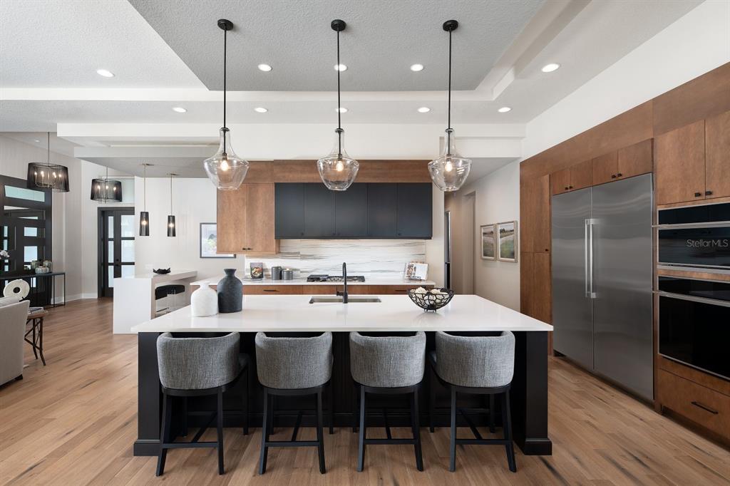 A modern kitchen features a large white island, dark cabinetry, wood accents, and pendant lighting — 0000 SE 47TH LOOP, OCALA, FL