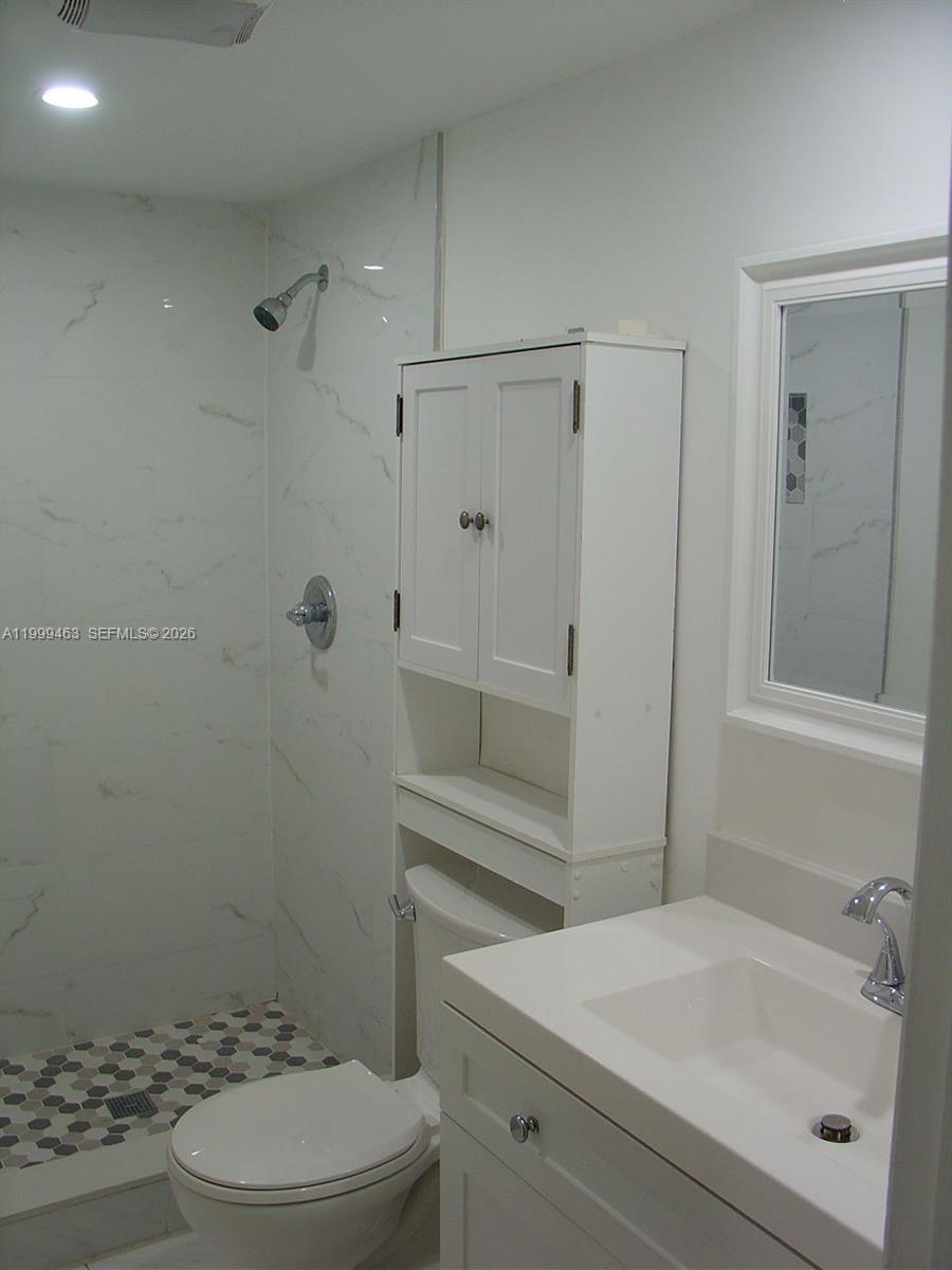 A bathroom features a white vanity, a toilet, and a walk-in shower with marble-look tiles — 19025 NW 62nd Ave # 202, Hialeah FL 33015, HIALEAH, FL
