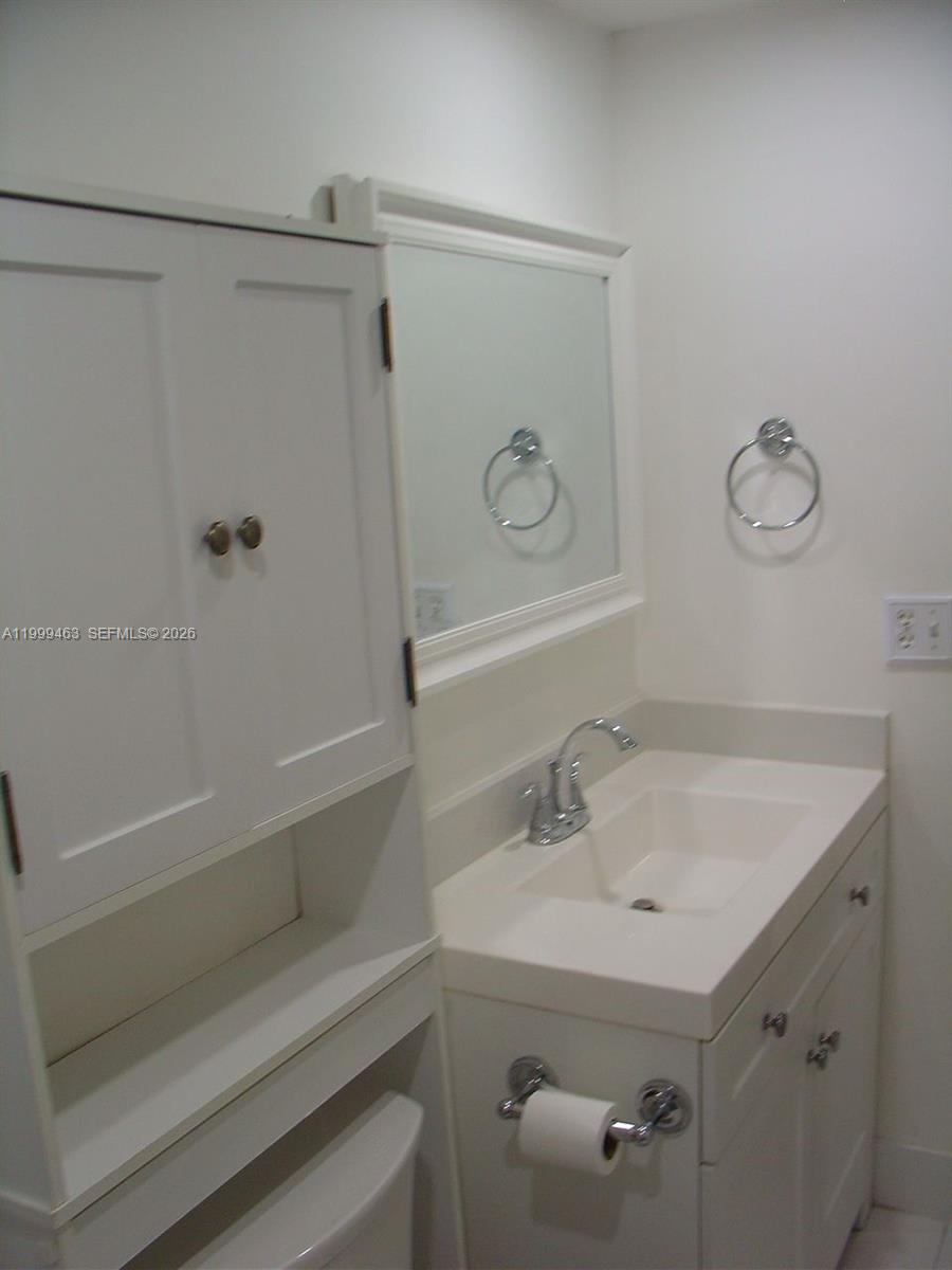 A white bathroom vanity with a sink, mirror, and adjacent storage cabinet — 19025 NW 62nd Ave # 202, Hialeah FL 33015, HIALEAH, FL