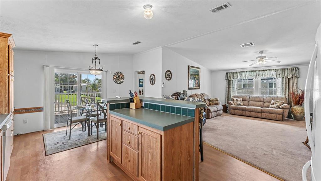 An open-concept kitchen with a wooden island and dining area adjacent to a carpeted living room — 525 PERCH PLACE, LAKELAND, FL