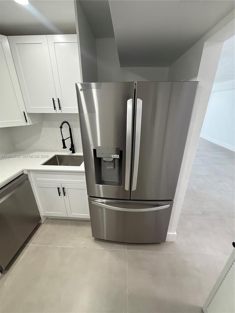 A stainless steel refrigerator stands next to a kitchen sink with white cabinets — 6937 Bay Dr, Miami Beach FL 33141, MIAMI BEACH, FL
