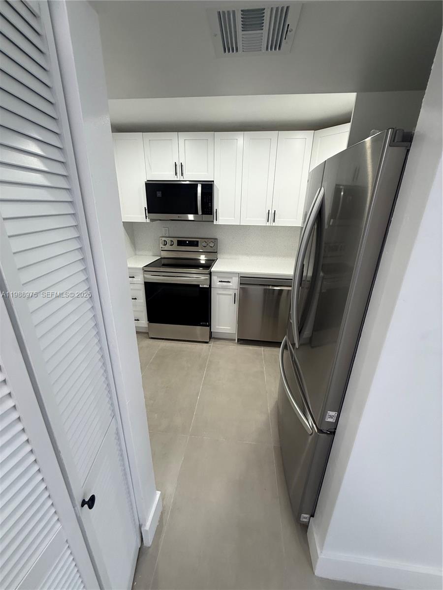 A galley kitchen features white cabinets, stainless steel appliances, and light-colored tile flooring — 6937 Bay Dr, Miami Beach FL 33141, MIAMI BEACH, FL