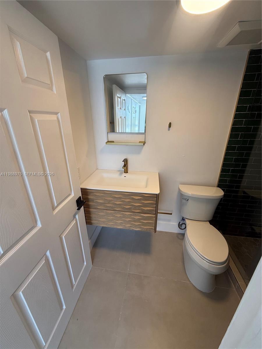A modern bathroom features a floating wood vanity, a white toilet, and dark green tile — 6937 Bay Dr, Miami Beach FL 33141, MIAMI BEACH, FL