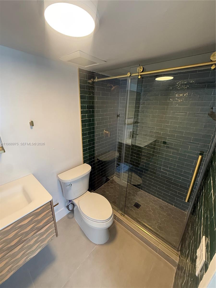 A bathroom features a glass-enclosed shower with dark green subway tiles and gold hardware — 6937 Bay Dr, Miami Beach FL 33141, MIAMI BEACH, FL