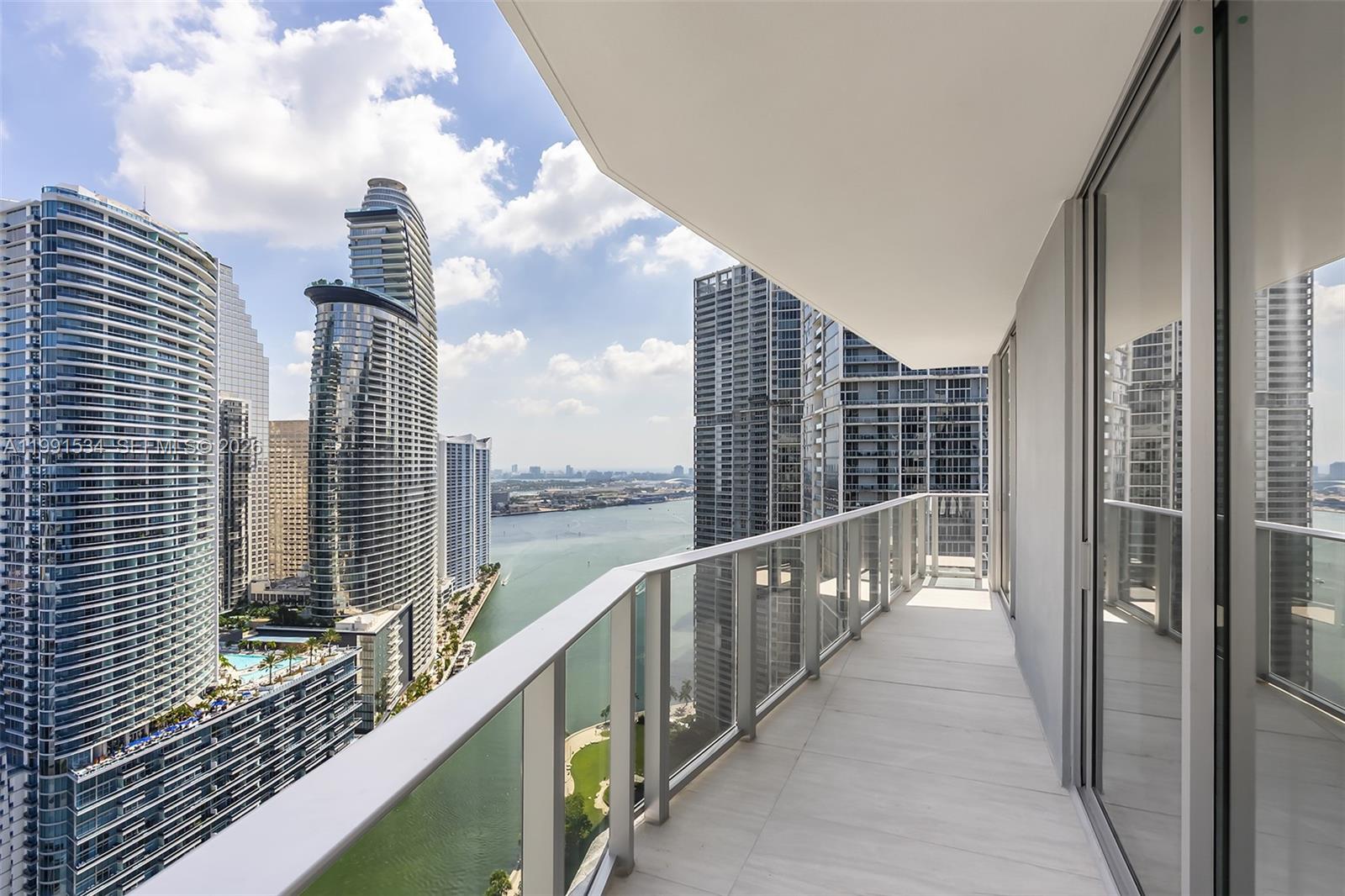 A high-rise balcony with glass railings overlooks a bay surrounded by modern skyscrapers — 77 SE 5th Street # 2403, Miami FL 33131, MIAMI, FL