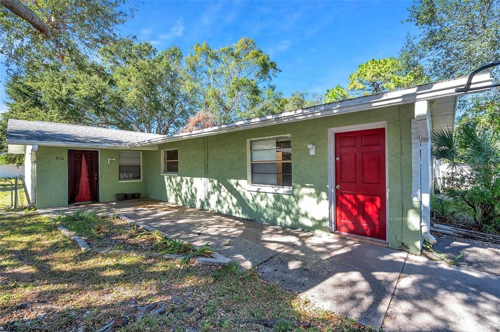 A single-story house with green stucco walls, two red doors, and a concrete patio — 914 LAKE PALMS DRIVE, LARGO, FL