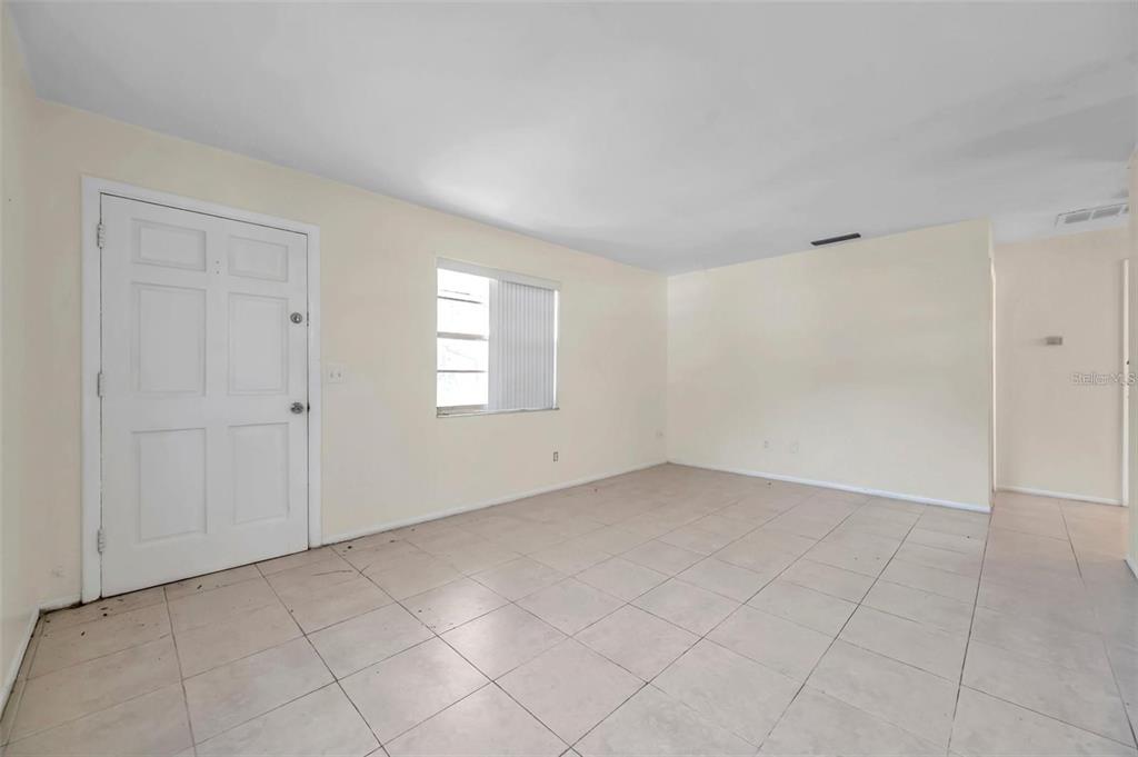 An empty room with light-colored walls, tiled flooring, a white front door, and a window — 914 LAKE PALMS DRIVE, LARGO, FL