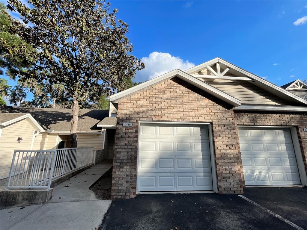 A brick-fronted residential building features two white garage doors and a concrete walkway with railings — 4700 SW ARCHER ROAD UNIT D30, GAINESVILLE, FL