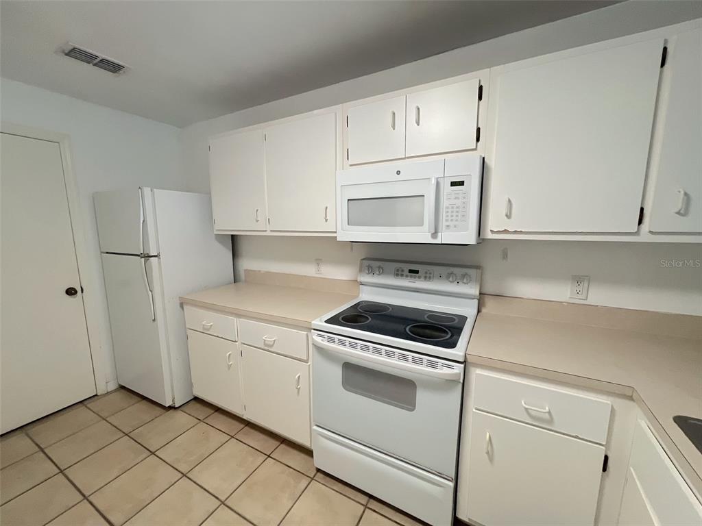 A kitchen featuring white cabinets, white appliances, beige countertops, and light-colored tile flooring — 4700 SW ARCHER ROAD UNIT D30, GAINESVILLE, FL