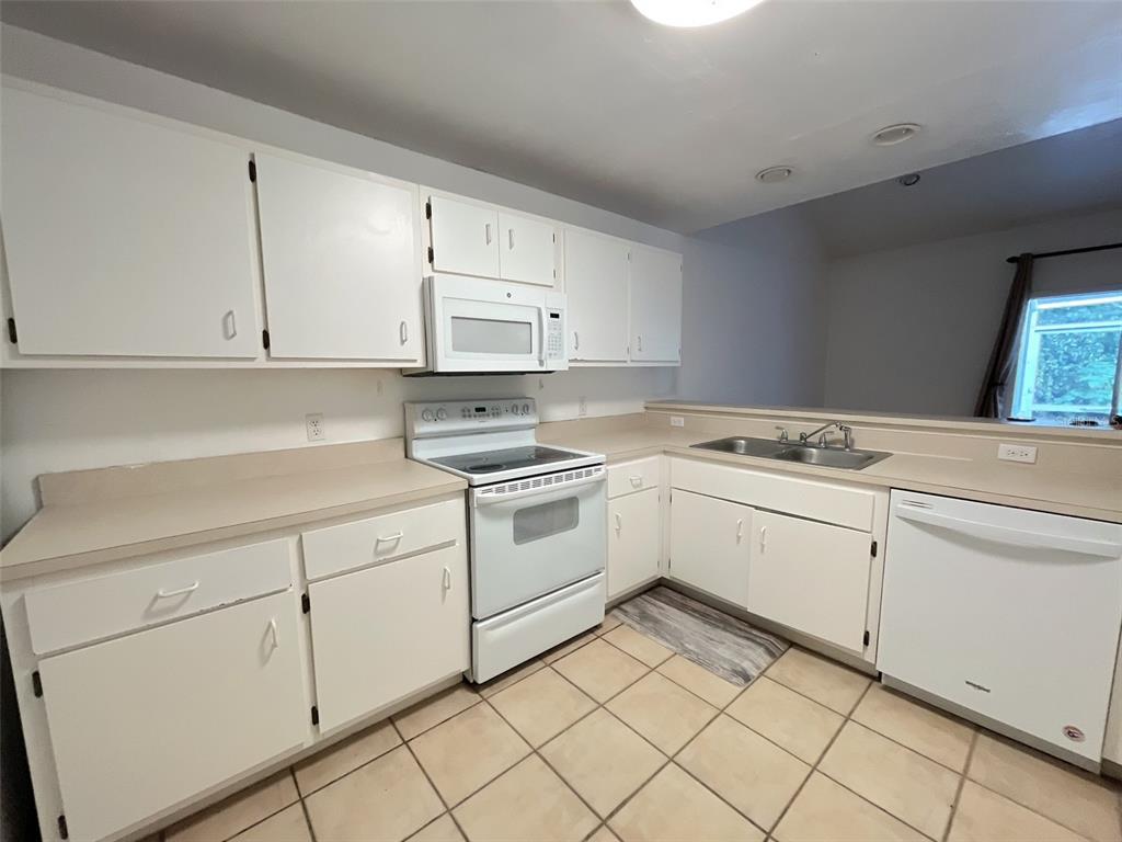 A kitchen features white cabinets, white appliances, beige countertops, and light-colored tile flooring — 4700 SW ARCHER ROAD UNIT D30, GAINESVILLE, FL