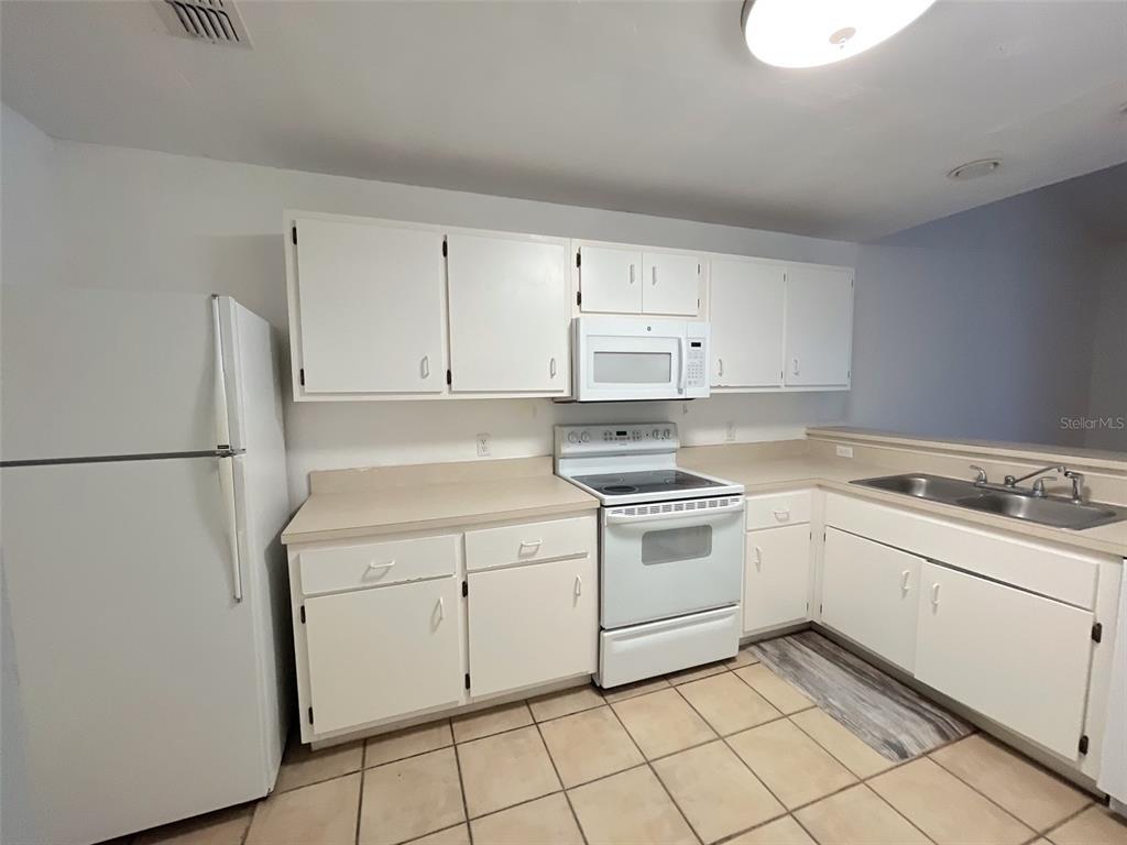 A kitchen features white cabinets, white appliances, beige countertops, and light-colored tile flooring — 4700 SW ARCHER ROAD UNIT D30, GAINESVILLE, FL