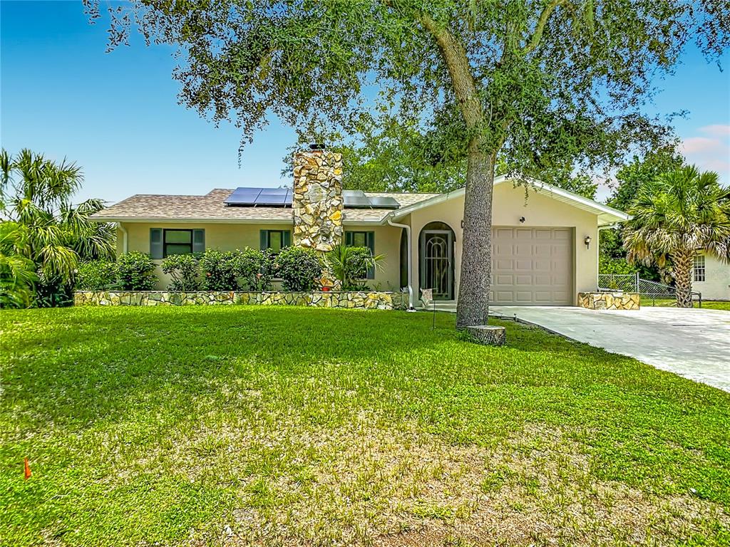 A single-story house with a stone chimney, solar panels, and a front-facing garage — 924 PHYLLIS TERRACE, PORT CHARLOTTE, FL