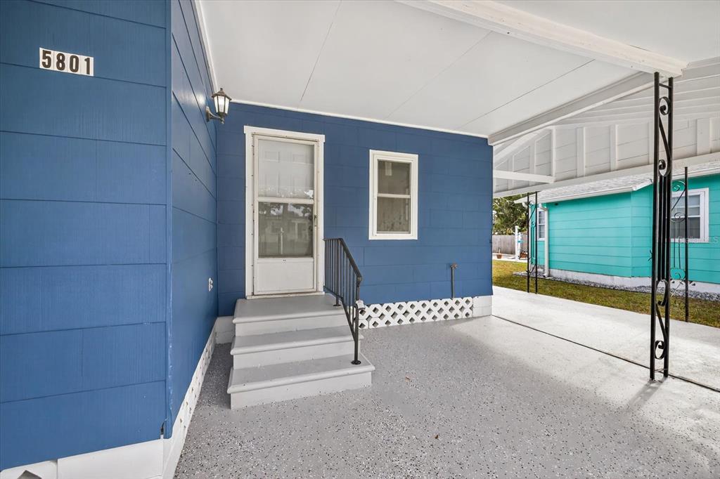A blue house exterior features a covered concrete porch, stairs, and a white storm door — 5801 MAGNOLIA STREET N, ST PETERSBURG, FL