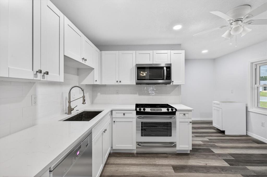 A modern kitchen features white shaker cabinets, stainless steel appliances, and light-colored quartz countertops — 5801 MAGNOLIA STREET N, ST PETERSBURG, FL