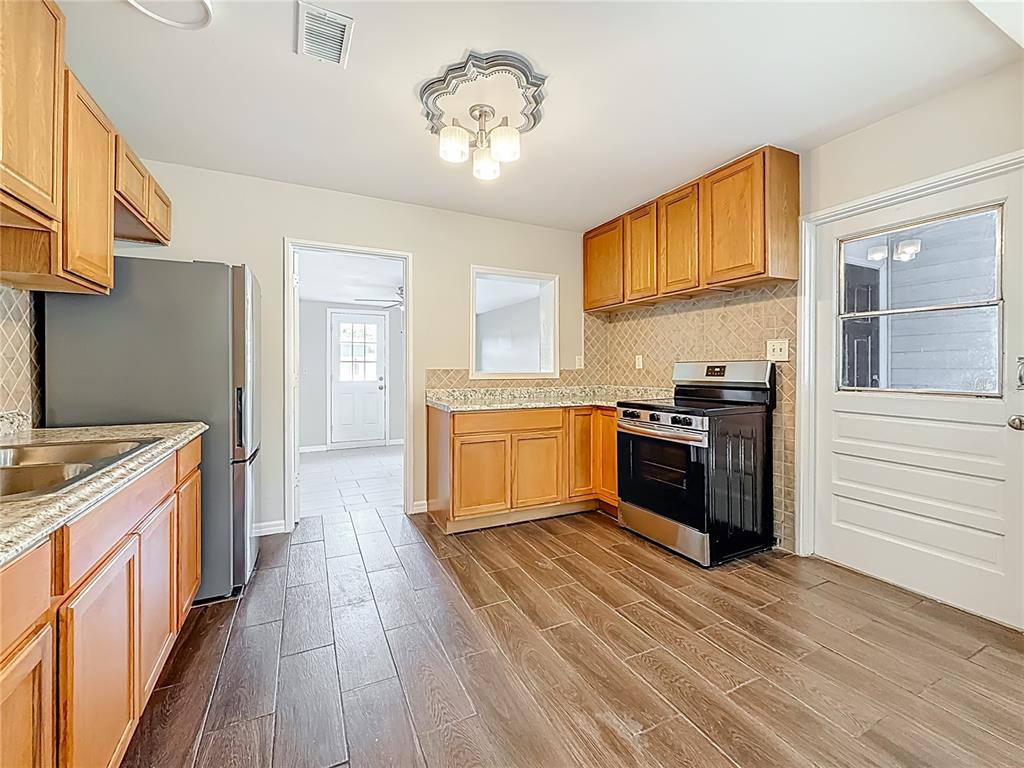 A kitchen features wood cabinets, granite countertops, stainless steel appliances, and wood-look tile flooring — 5051 AVERY ROAD, NEW PORT RICHEY, FL