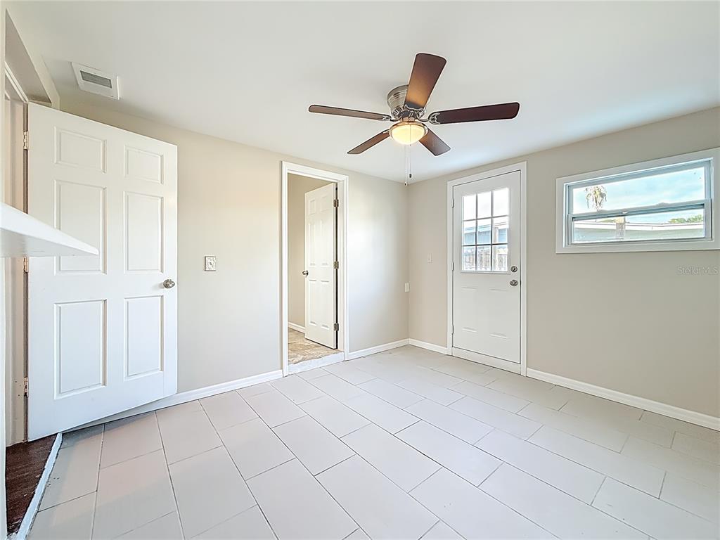 A room with light-colored tile flooring, a ceiling fan, two white doors, and a window — 5051 AVERY ROAD, NEW PORT RICHEY, FL