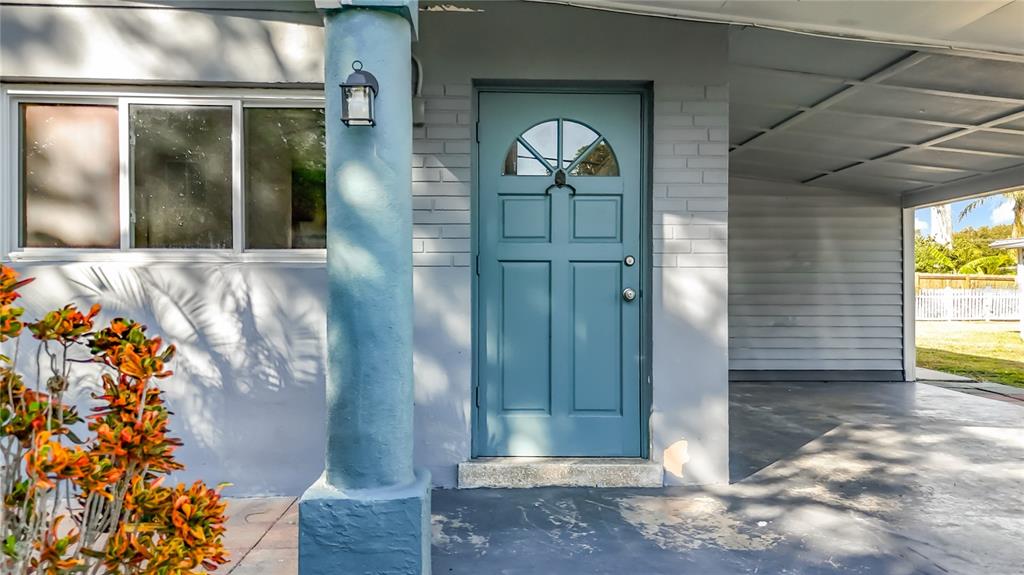A blue front door is situated next to a window and a covered carport area — 5051 AVERY ROAD, NEW PORT RICHEY, FL