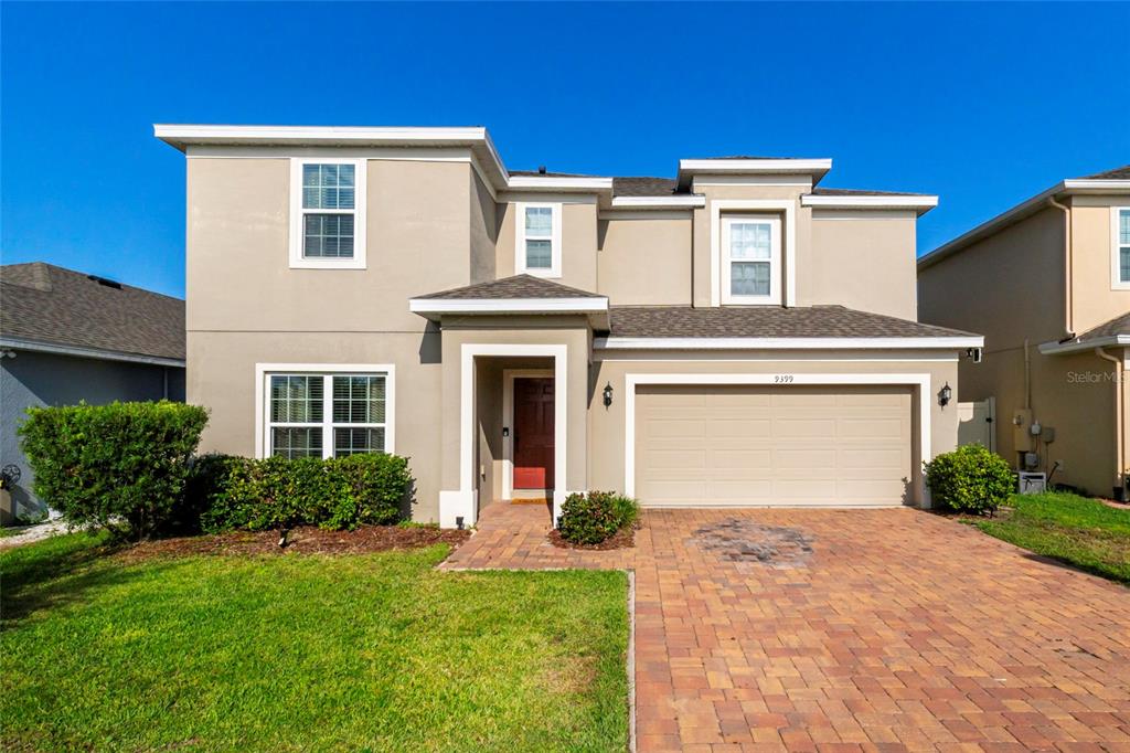 A two-story suburban house with a tan stucco exterior, a brick driveway, and a garage — 9399 VILLANOVA DRIVE, GROVELAND, FL