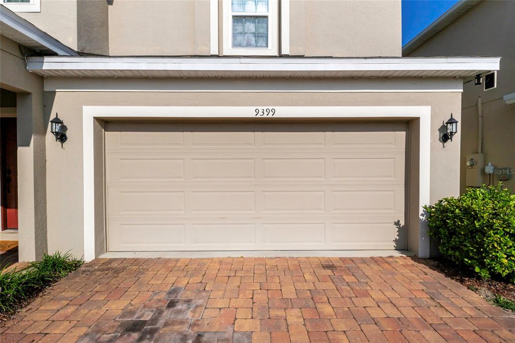 A beige two-car garage door with a brick paver driveway in front — 9399 VILLANOVA DRIVE, GROVELAND, FL